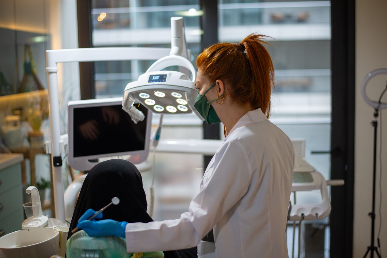 A dentist wearing a mask attends to a patient in a modern dental clinic with advanced equipment.